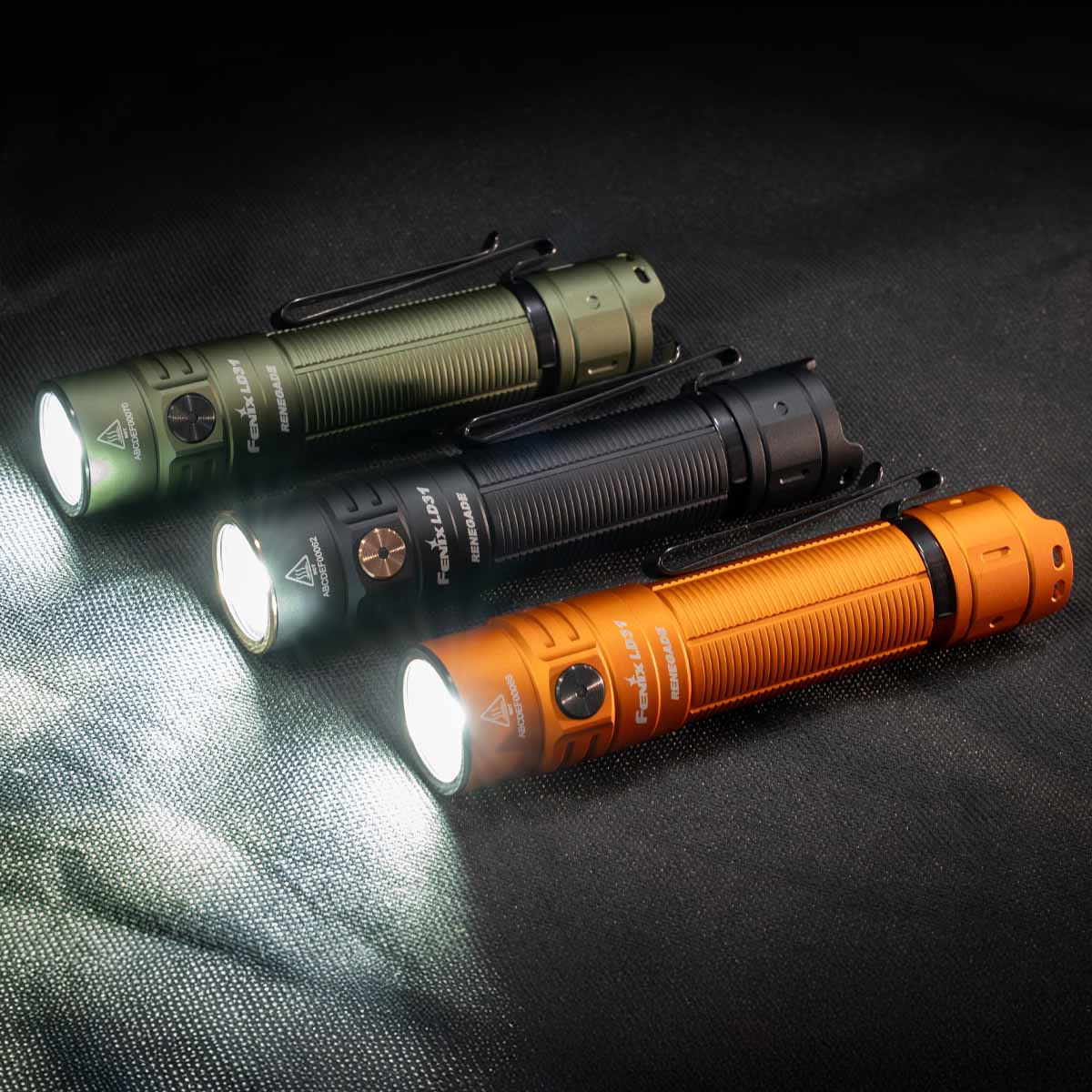 Three ld31 renegade flashlights in green, black, and orange on a dark textured surface.